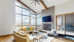 A spacious living room with a large window, a fireplace, a sofa, and a television. - Luxury home w/ private hot tub, great views & convenient location (Winter Park)