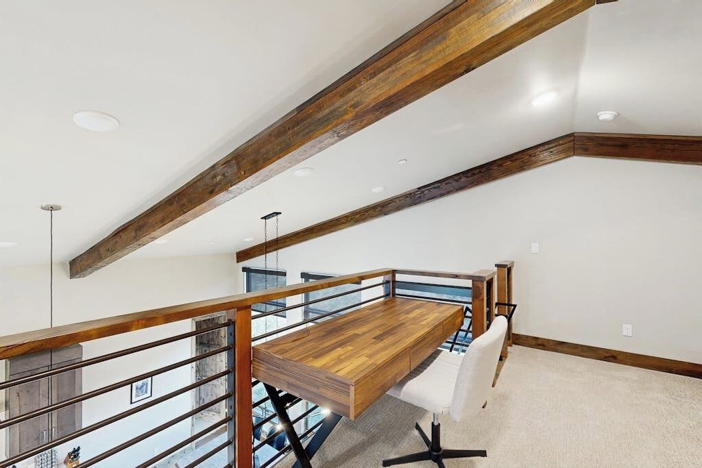 Un moderno espacio tipo loft con vigas de madera a la vista, una mesa de madera alargada y una silla blanca.