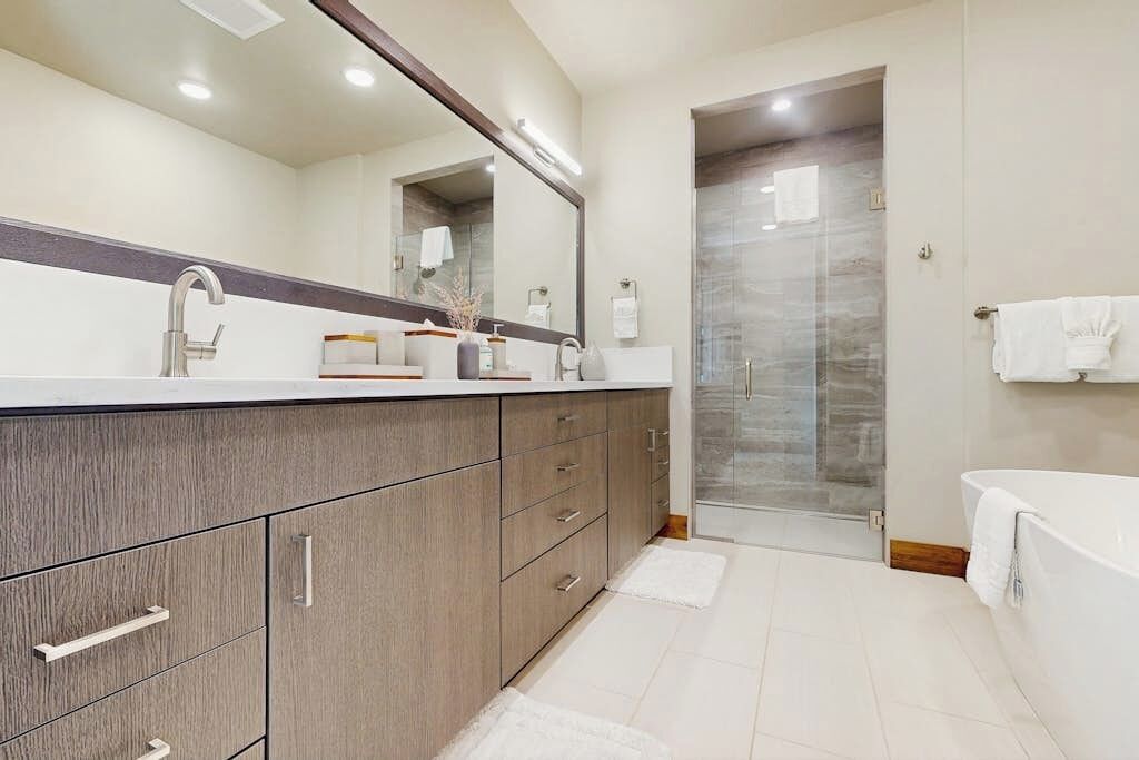 A modern bathroom with a large mirror, a sink, a bathtub, and a shower area.