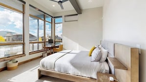 A modern bedroom with a large bed, a desk, and a view of the city. - Luxury home w/ private hot tub, great views & convenient location (Winter Park)