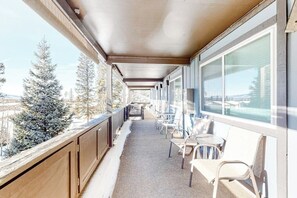 Ein überdachter Balkon mit Stühlen und Tischen, große Fenster und Blick auf schneebedeckte Bäume.