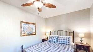 Ein Schlafzimmer mit einem Bett, einem Deckenventilator, einem Nachttisch mit Lampe und einer gerahmten Karte an der Wand.
