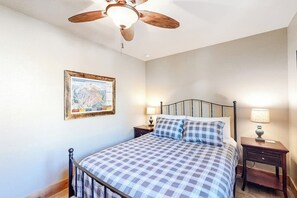 Ein Schlafzimmer mit einem Bett, einem Deckenventilator, einem Nachttisch mit Lampe und einer gerahmten Karte an der Wand.