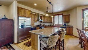 A kitchen with wooden cabinets, a stainless steel refrigerator, a granite island, and hanging pendant lights. - Spacious home w/ kitchen, wifi, great views, deck & convenient location (Winter Park)