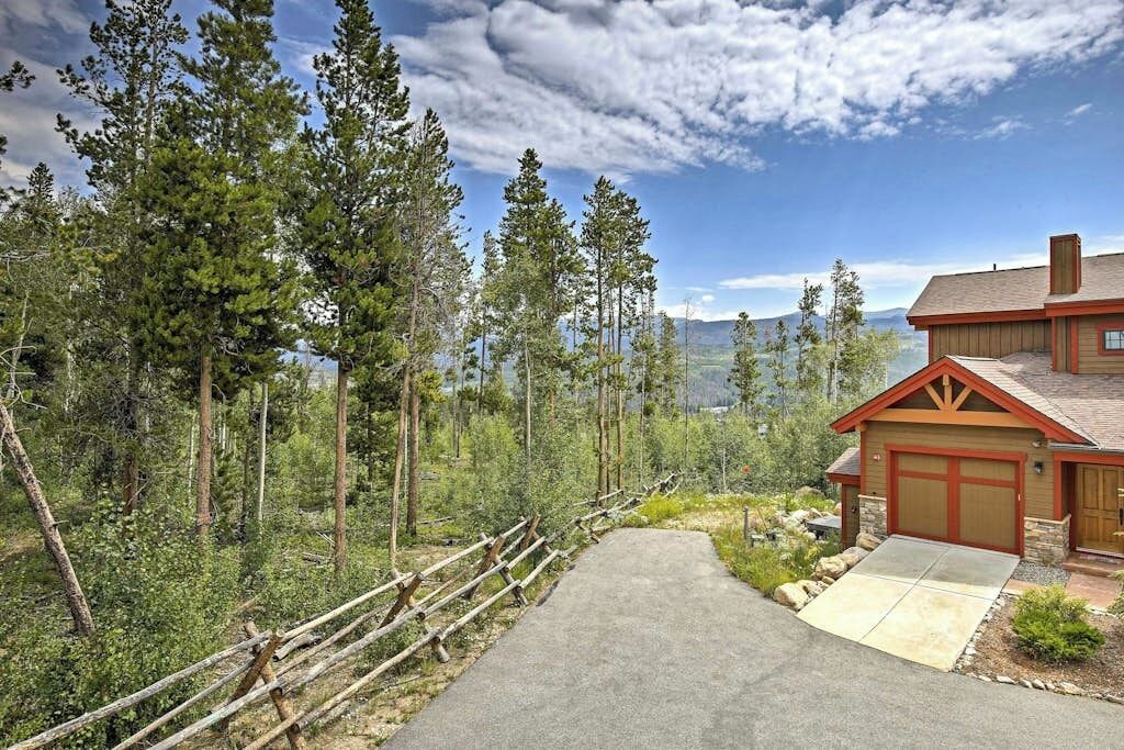 A house with a garage, surrounded by a forest and mountains.