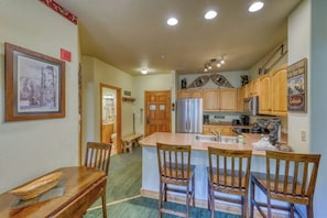A kitchen with wooden cabinets, a central island with bar stools, a refrigerator, and a microwave. - Walk to the Slopes, Amazing Ski Area Views, Shared Hot Tubs Too (Keystone)