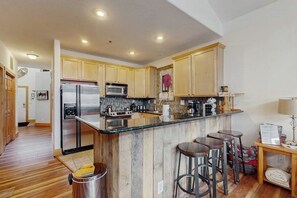A modern kitchen with wooden cabinets, stainless steel appliances, and a central island with stools. - Sunny & Spacious Condo in Downtown Dillon, Fireplace, WiFi (Dillon)