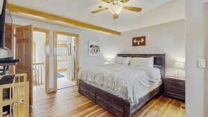Un dormitorio con una cama de madera, un ventilador de techo, un televisor y un armario de madera.