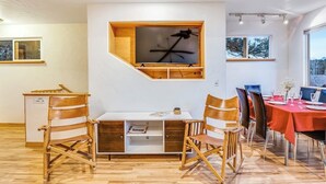 Ein Essbereich mit Holztisch, Stühlen und einem fest installierten Fernseher.