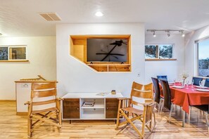 Ein Essbereich mit Holztisch, Stühlen und einem fest installierten Fernseher.