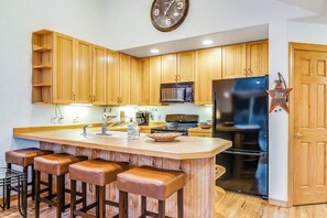 Eine Küche mit Holzausstattung, einer zentralen Kochinsel mit Barhocker, einer Mikrowelle, einem Herd und einem Kühlschrank.