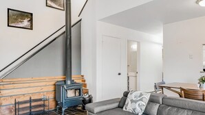 A living room with a sofa, a wooden bench, a fireplace, a staircase, and a dining area. - Two-Level Condo w/ Mountain View, Wood Stove, WiFi, Laundry & Central Location (Pagosa Springs)