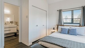 A bedroom with a bed, bedside table, lamp, and a window with curtains. - Two-Level Condo w/ Mountain View, Wood Stove, WiFi, Laundry & Central Location (Pagosa Springs)