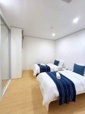 A hotel room with two beds, a shower area, and a wooden floor.