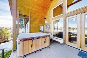 Eine Holzterrasse mit Whirlpool, einer Sitzbank und einer Glastür zu einem Außenbereich.