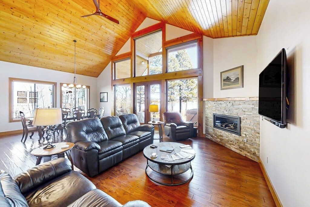 A spacious living room with a high ceiling, a fireplace, leather sofas, a coffee table, and a TV mounted on the wall.