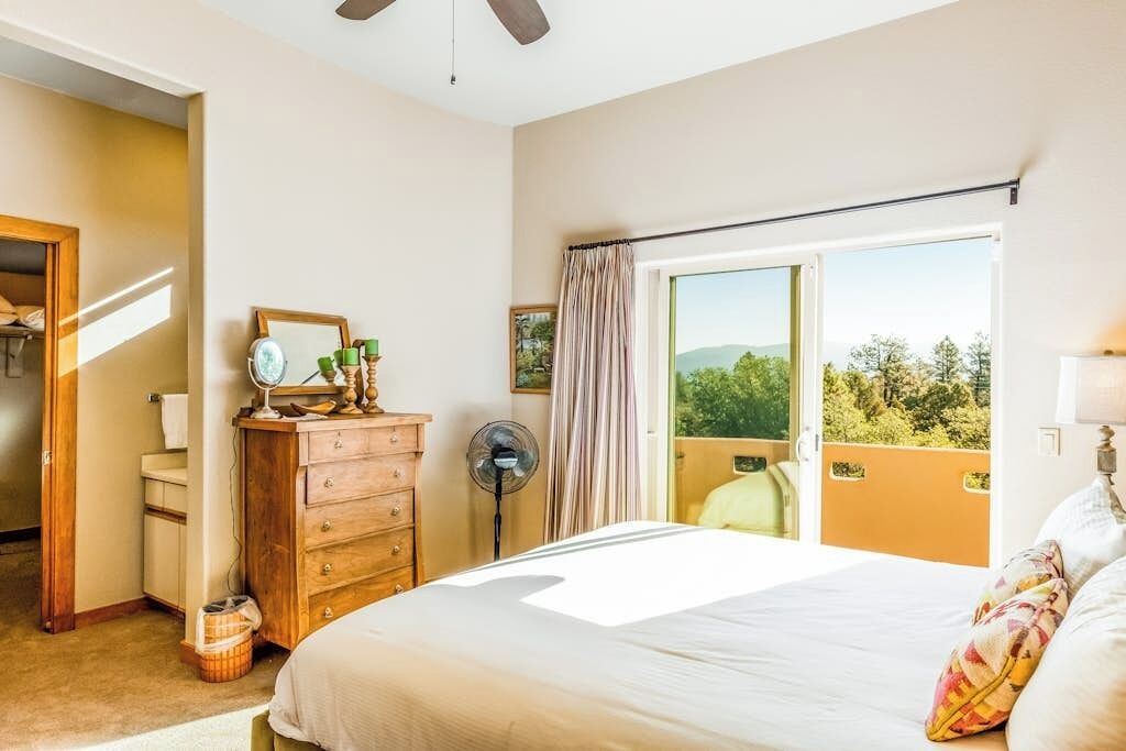 A bedroom with a bed, dresser, mirror, and a balcony with a view.