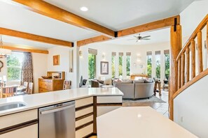 Eine moderne Küche mit Geschirrspüler, ein Essbereich mit Tisch und Stühlen, ein Wohnzimmer mit Sofa und eine Treppe mit Holzläufungen.