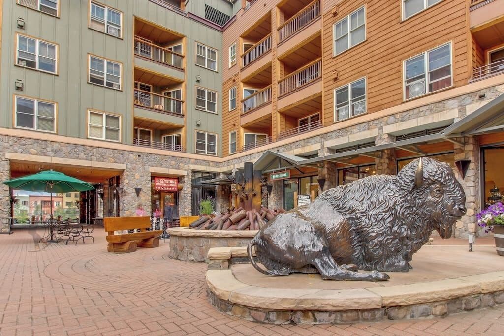 A multi-story building with balconies, a central courtyard with a sculpture, outdoor seating, and a stone facade.