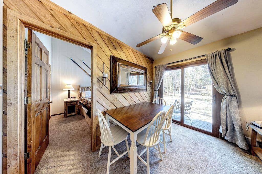 Una habitación con techo de madera, una mesa de comedor con sillas, un ventilador de techo y vistas a través de un ventanal.