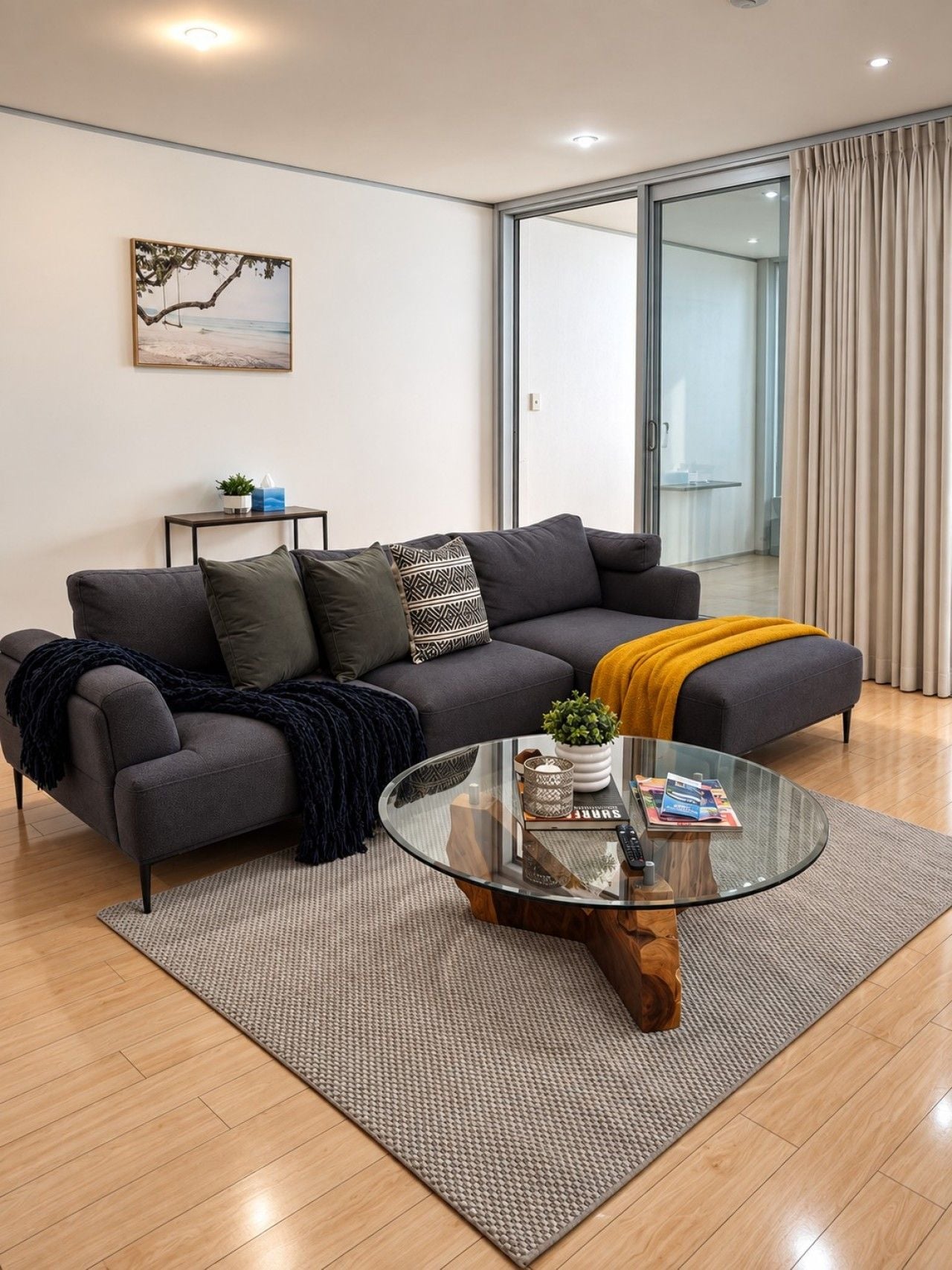 Un salon moderne avec un canapé gris, une table basse en verre et une petite table d’appoint agrémentée d’une plante.