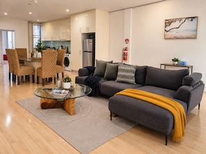 Ein modernes Wohnzimmer mit einem grauen Sofa, einem Glastisch und einem Essbereich mit Korbstühlen.