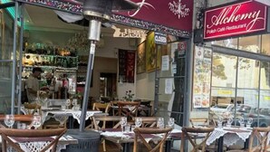 An outdoor dining area with wicker chairs and tables, a large decorative heater, and a sign for Alchemy Polish Café Restaurant. - Downtown Cozy Retreat by Central Station (Surry Hills)