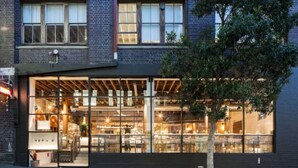 A modern building with large glass windows, a visible interior with tables and chairs, and a tree in front. - Downtown Cozy Retreat by Central Station (Surry Hills)