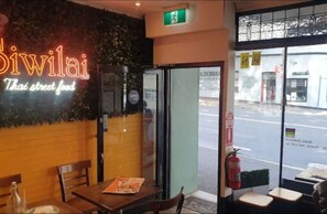 A restaurant named 'Siwilai Thai street food' with a neon sign, a glass door entrance, and a view of the street outside. - Downtown Cozy Retreat by Central Station (Surry Hills)