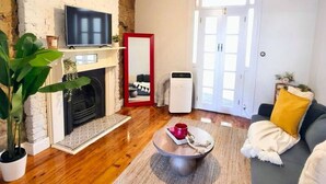 Ein Wohnzimmer mit Kamin, Fernseher, Sofa, Couchtisch und einem großen Fenster.
