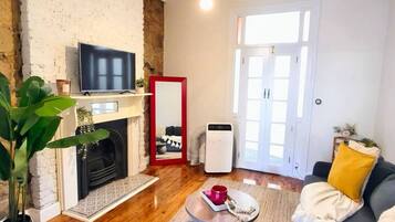 Ett vardagsrum med en öppen spis, en tv, en soffa, ett soffbord och ett stort fönster.