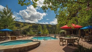 A pool area with lounge chairs and umbrellas, surrounded by trees and a mountain view.