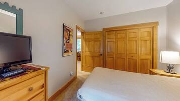 A bedroom with a bed, a dresser, a television, a wooden wardrobe, and a door leading to another room.