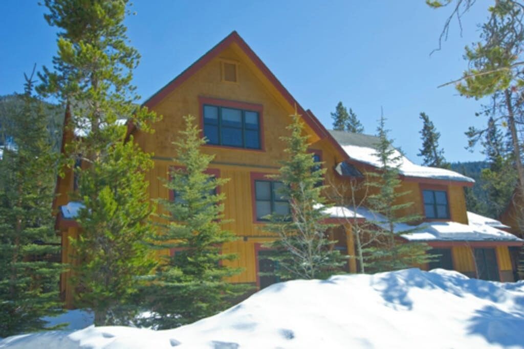 A wooden cabin with a triangular roof, surrounded by snow and trees.