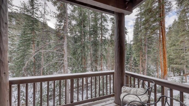 A wooden deck with metal chairs, overlooking a forested area with tall trees.