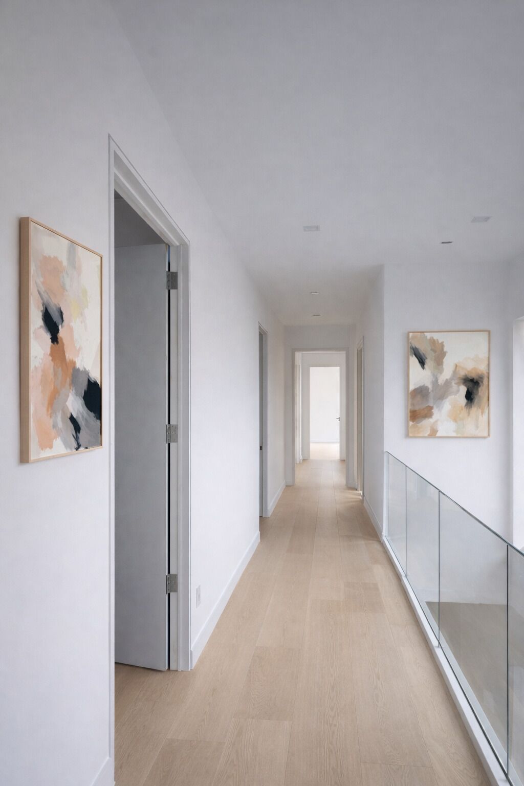 A modern hallway with a wooden floor, white walls, and abstract paintings.