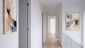 Un couloir moderne avec un plancher en bois, des murs blancs et des tableaux abstraits.