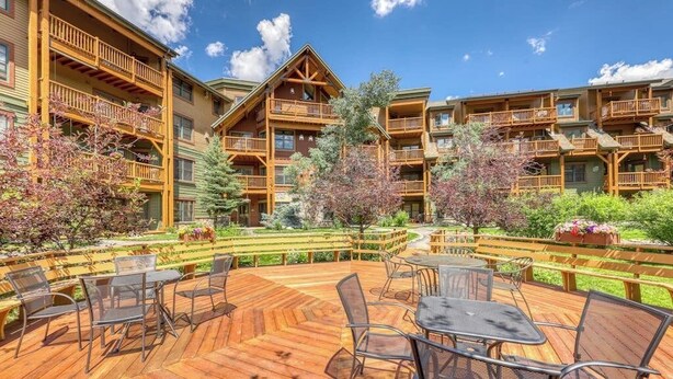 Une terrasse en bois, agrémentée de mobilier d’extérieur, entourée d’immeubles à plusieurs étages dotés de balcons.