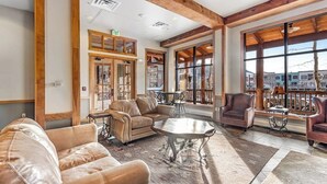 A spacious living area with leather sofas, a coffee table, and a view through large windows. - Spacious, resort condo w/private balcony, shared pool & hot tub. Walk to slopes (Keystone)