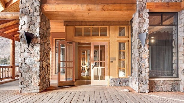 A wooden deck with stone pillars, a glass door entrance, and a view of the interior. - Spacious, resort condo w/private balcony, shared pool & hot tub. Walk to slopes (Keystone)