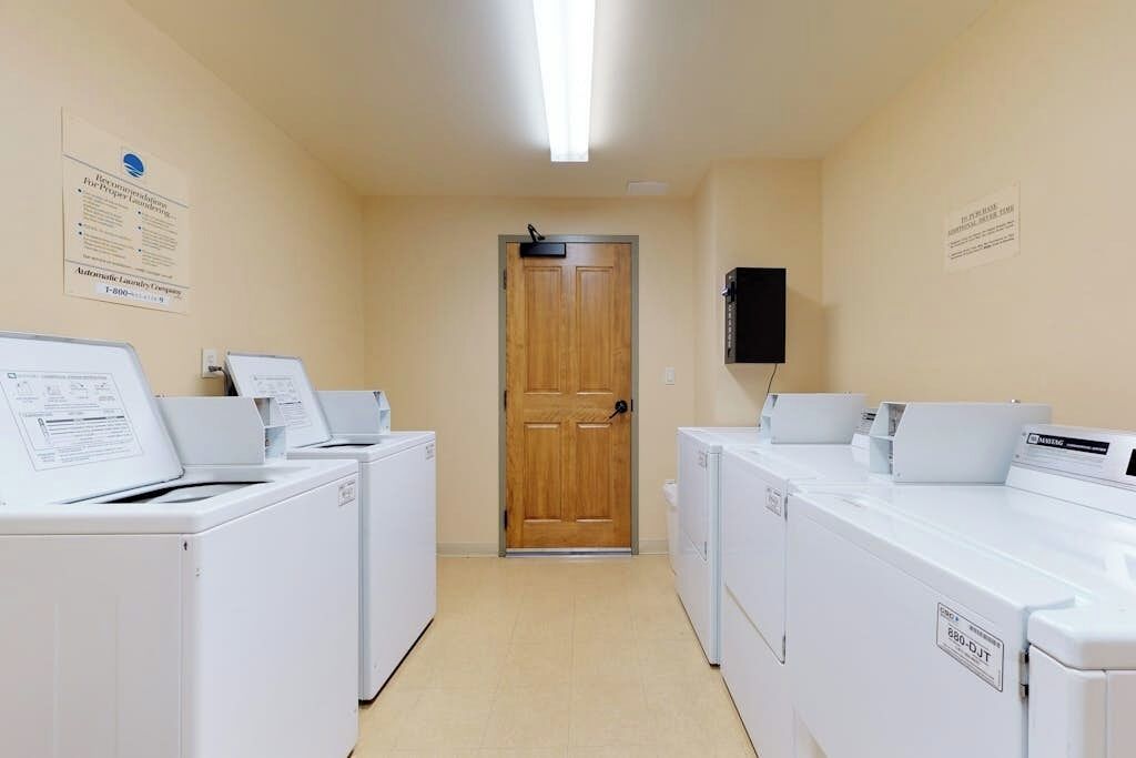 A laundry room with multiple washing machines, a wooden door, and informational posters on the walls.
