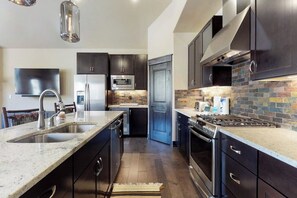 A modern kitchen with dark cabinetry, stainless steel appliances, a granite countertop, and a tiled backsplash. - Newly built townhome with hot tub, decks & gas fireplace - walk to lifts (Keystone)