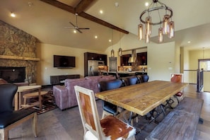 A spacious living area with a stone fireplace, a dining table with chairs, a sofa, and a kitchen in the background. - Newly built townhome with hot tub, decks & gas fireplace - walk to lifts (Keystone)