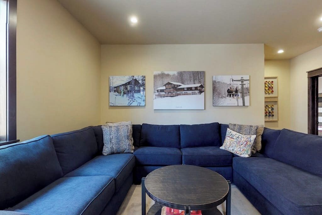 Un salon avec un canapé d’angle bleu foncé, une table basse ronde et trois photographies encadrées accrochées au mur.