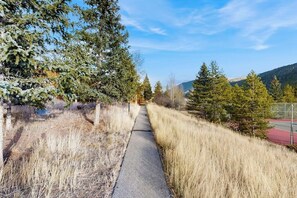 Ein gepflasterter Weg, der von trockenem Gras und Bäumen gesäumt wird und zu einer fernen Bergkette führt.