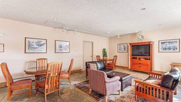 A living room with a stone floor, wooden furniture, a television, and framed pictures on the walls.