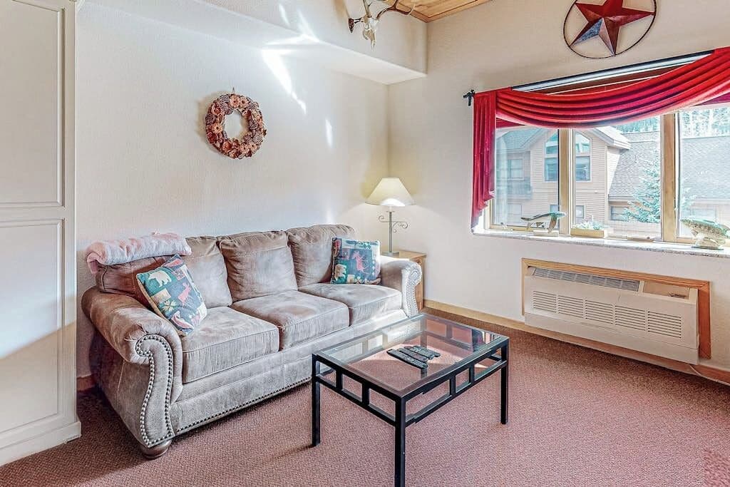 A living room with a sofa, a glass coffee table, a lamp, a window with red curtains, and a star decoration on the wall.