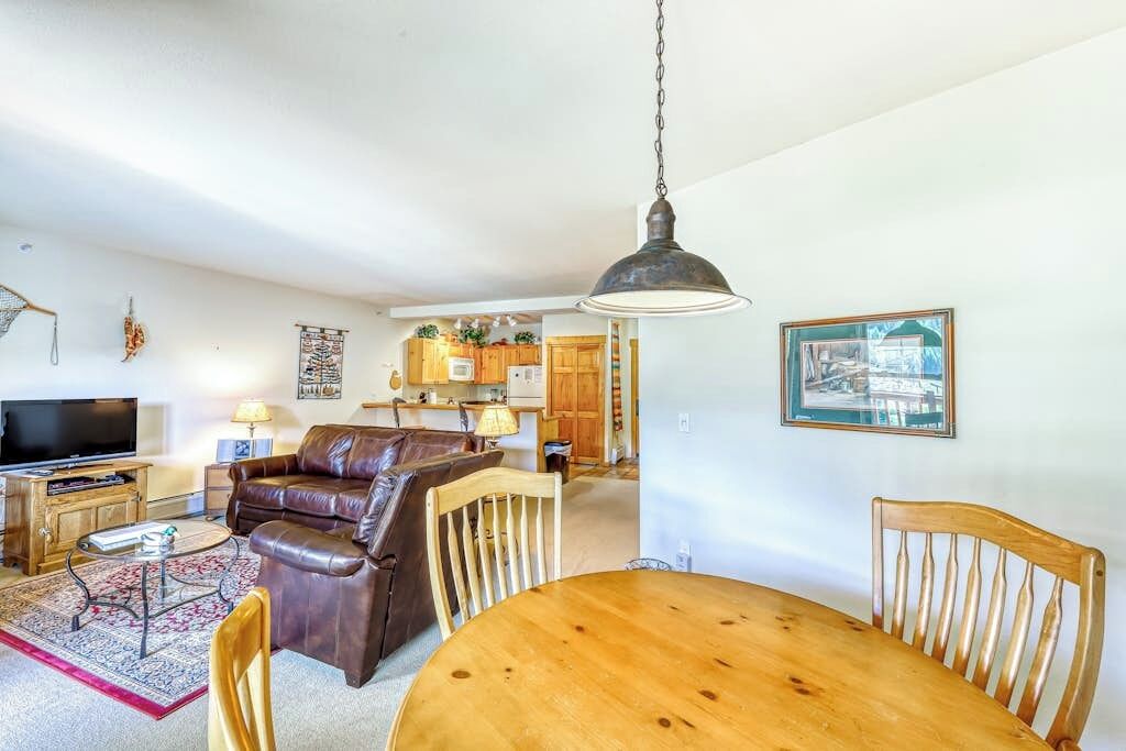Ein Wohnzimmer mit Fernseher, Ledersofa, Esstisch aus Holz und Stühlen.
