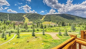 Ett bergigt landskap med en träveranda som vetter ut mot en dal med ett skidområde och ett hotell.