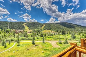 Eine gebirgige Landschaft mit einer Holzterrasse mit Blick auf ein Tal, in dem ein Skigebiet und eine Lodge liegen.